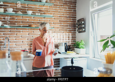 Older Caucasian woman using cell phone in kitchen Stock Photo