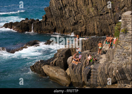 A group of Italians sunbathe on the rocky ocean cliffs in Cinqu Terre, Italy. Stock Photo