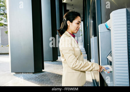 Asian businesswoman using ATM outdoors Stock Photo