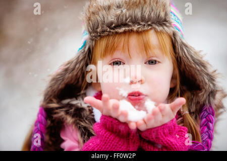 Caucasian girl blowing handful of snow Stock Photo