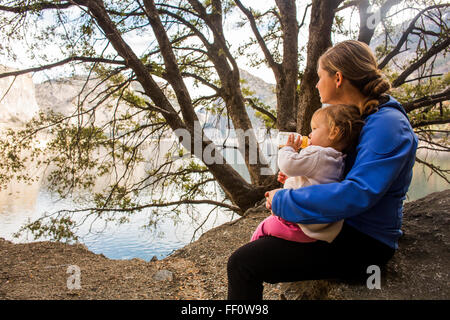 Caucasian mother and daughter sitting at lake Stock Photo
