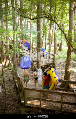 A group of people carry their inflatable rafts along a boardwalk in the Florida woods on their way to float down the river. Stock Photo