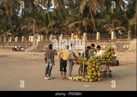 A group of young men gathered around a coconut vendor on Juhu Beach in Mumbai, India. Stock Photo