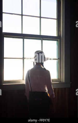 A woman in a hat looks quietly out the window. Stock Photo