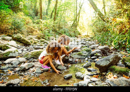 Mixed race sisters exploring stream Stock Photo