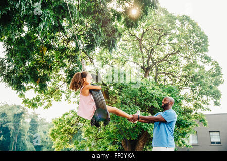 Father pushing daughter on tire swing Stock Photo