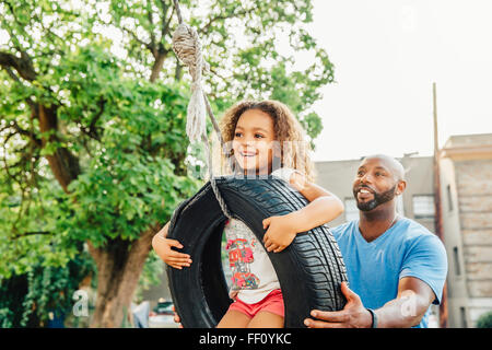 Father pushing daughter on tire swing Stock Photo