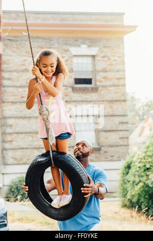 Father pushing daughter on tire swing Stock Photo