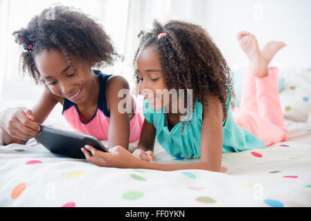 Mixed race sisters using digital tablet on bed Stock Photo