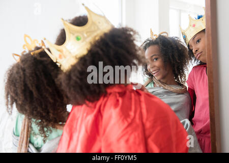 Mixed race sisters playing dress up in mirror Stock Photo