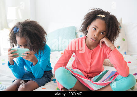 Bored mixed race girl sitting on bed Stock Photo