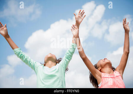 Mixed race sisters cheering in blue sky Stock Photo