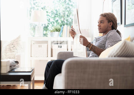 Mixed race man reading newspaper on sofa Stock Photo