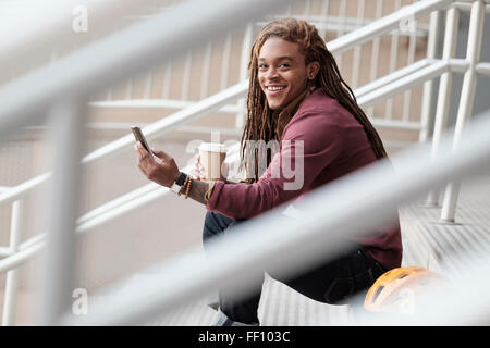 Mixed race man using cell phone on staircase Stock Photo