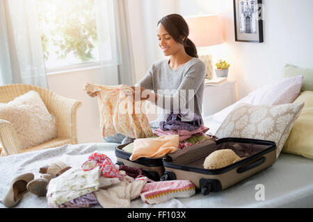 Mixed race woman packing suitcase in bed Stock Photo