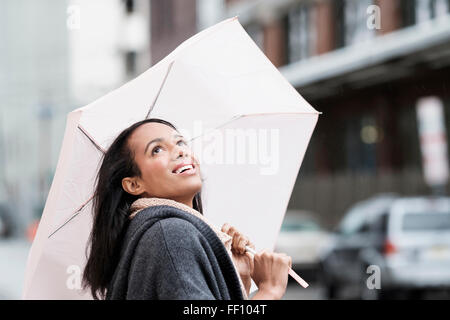 Mixed race woman carrying umbrella outdoors Stock Photo