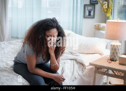 Sad Black woman sitting on bed Stock Photo