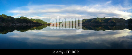Mirror-like panorama of Triangle Lake, Oregon, USA with green hills, blue sky and wispy white clouds Stock Photo