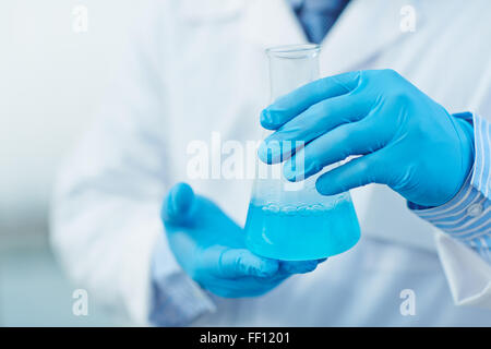 Modern scientist in protective gloves holding tube with blue fluid Stock Photo