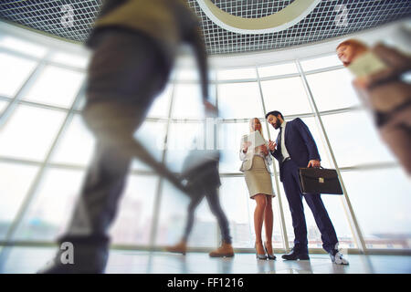 Two business partners discussing data in corridor among walking people Stock Photo