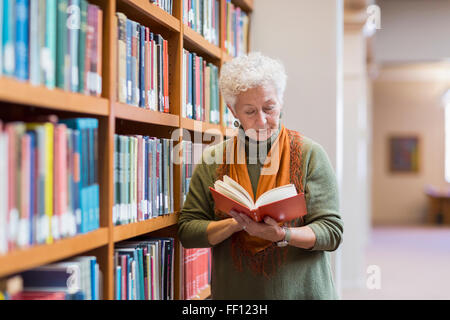 Older mixed race woman reading book in library Stock Photo