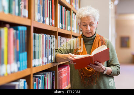 Older mixed race woman reading book in library Stock Photo