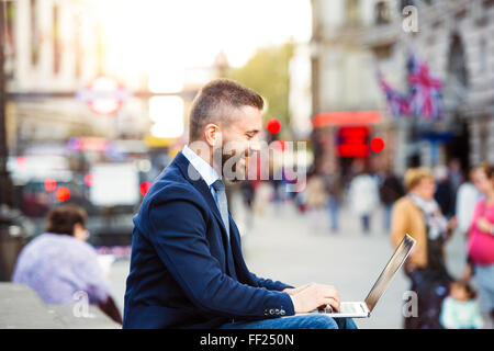 Hipster manager working on laptop on sunny Piccadilly Circus, Lo Stock Photo