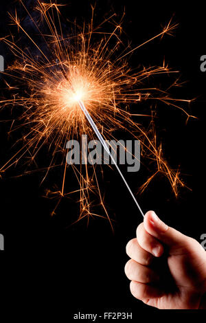 Child's hand, holding a burning sparkler on the black background. Stock Photo