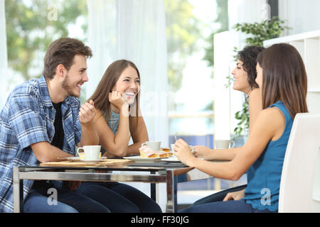 Group of 4 happy friends meeting and talking and eating desserts on a table at home Stock Photo