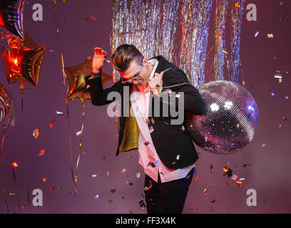 Happy handsome man in sunglasses holding disco ball and dancing alone over purple background Stock Photo