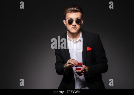 Man in trendy cloth holding box with a proposal ring over black background Stock Photo
