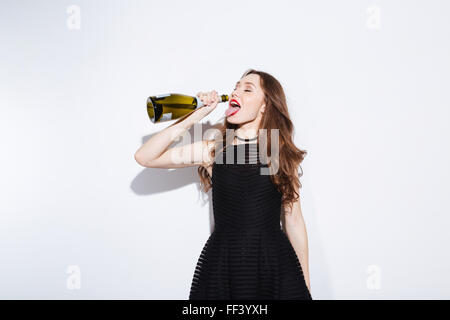 Woman in black dress drinking champagne from bottle isolated on a white background Stock Photo
