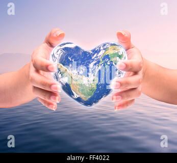 World in heart shape with over women human hands on blurred natural background blue cyan turquoise tree and sky: World Heart hea Stock Photo
