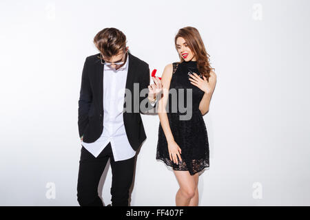Handsome shy young man giving an engagement ring to his girlfriend over white background Stock Photo