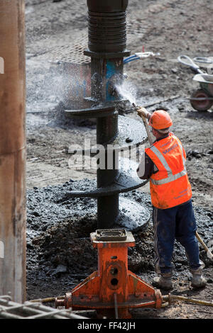 Installing Geothermal International’s ‘Energy Pile’ ground source heat pumps at a building in the City of London. One of the workers cleans the drill before it goes back in the ground. Stock Photo