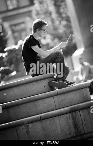 Young man sitting and smoking in the public square Royal garden Kungsträdgården on a summer day in downtown Stockholm,Sweden Stock Photo