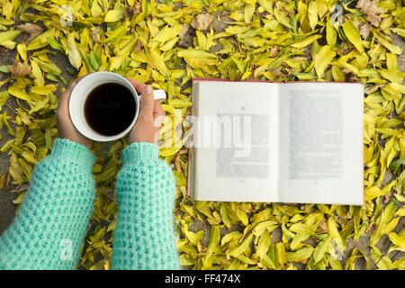 Woman hands holding cup of coffee over leaves background. top view Stock Photo
