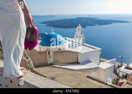 Bride with a  shoes  in his hands stands high over the coast. Santorini, Greece. Stock Photo