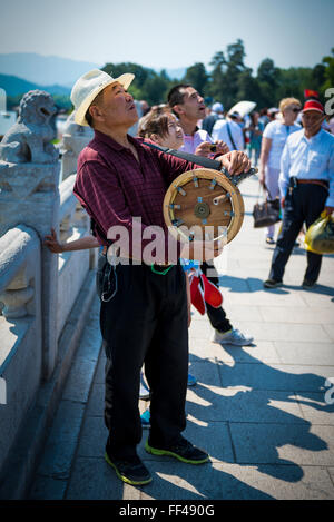 chinese man flying a kite on the bridge of the summer palace, Beijing. sunny good mood with handmade wheel, people watching. Stock Photo