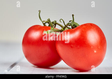 Two red ripe tomatos on a white wooden table. Isolated macro shot in high key. Stock Photo