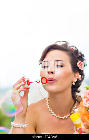 Beautiful bride blowing soap bubbles outdoors Stock Photo