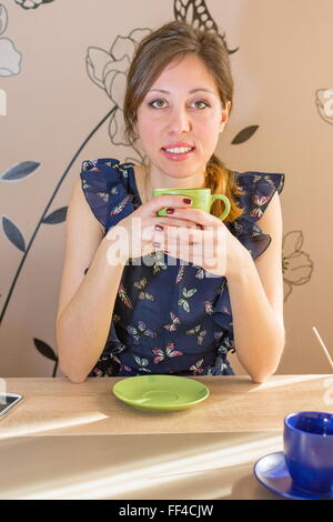 Smiling brunette drinking coffee at the kitchen table Stock Photo