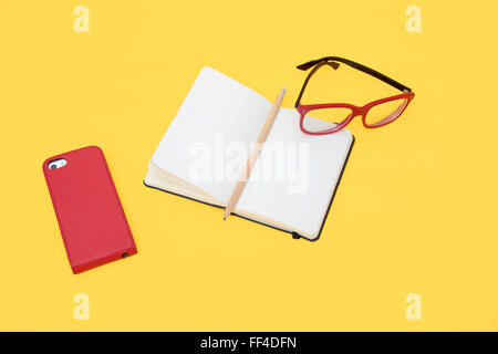 Eyeglasses, smartphone and notebook isolated on yellow background Stock Photo
