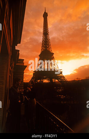 Couple on apartment balcony enjoying sunset drink under dramatic sky near Eiffel Tower in Paris Stock Photo