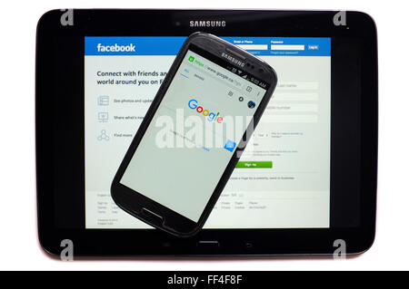 The Google page on a smartphone and the Facebook log in page on a tablet photographed against a white background. Stock Photo