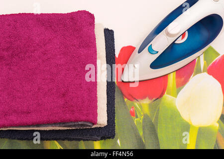 Electric iron and towels on ironing board Stock Photo
