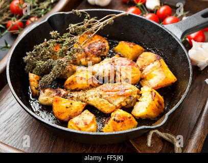 Roasted chicken legs with baked potatoes garnish and herbs in a cooking pan Stock Photo