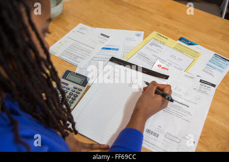 A young lady sits at her kitchen table at home checking over the household bills. Dealing with debt. Household utility bills making it difficult for a British home owner to afford. Difficulty paying gas and electricity bills is common as the economic downturn makes personal finances feel the pinch. London, UK. Stock Photo