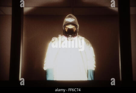 A man wearing a hazardous material protective clean suit, a hasmat suit, standing behind window Stock Photo