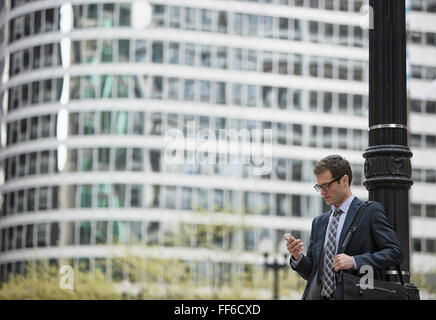 A working day. Businessman in a work suit and tie on a city street, checking his phone. Stock Photo